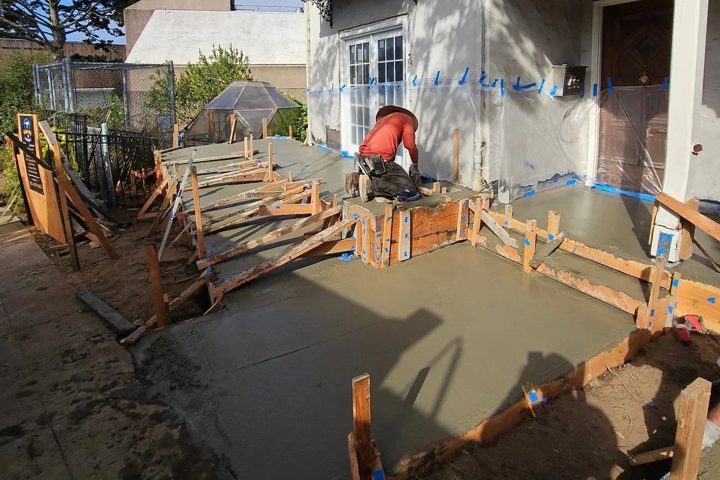 Hand-finishing the wet concrete ramp against the building, formwork and blue tape — ADA Ramp & Sidewalk — West Portal, West Portal, San Francisco