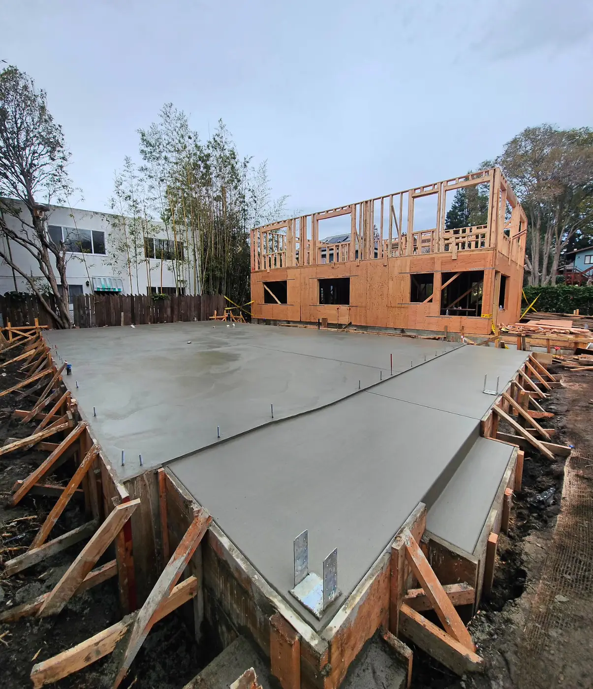 Fresh smooth slab w/ anchor bolts, framed ADU behind — ADU Foundations — Two Projects, SF Bay Area