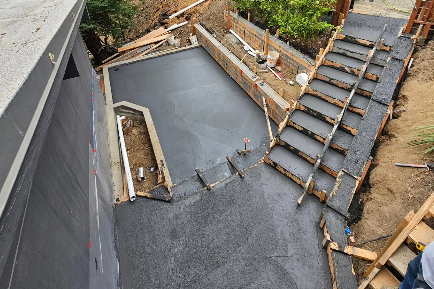 Aerial poured dark slab + stair forms, wet — Hillside Outdoor Living Transformation, Oakland, CA