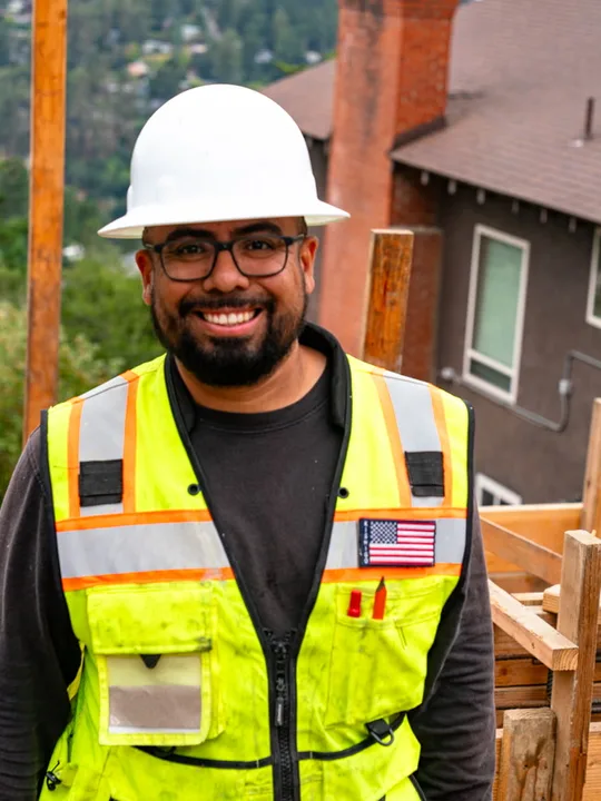 Jose Rosales, founder of New Edge Concrete, on a hillside job site in a hard hat and safety vest