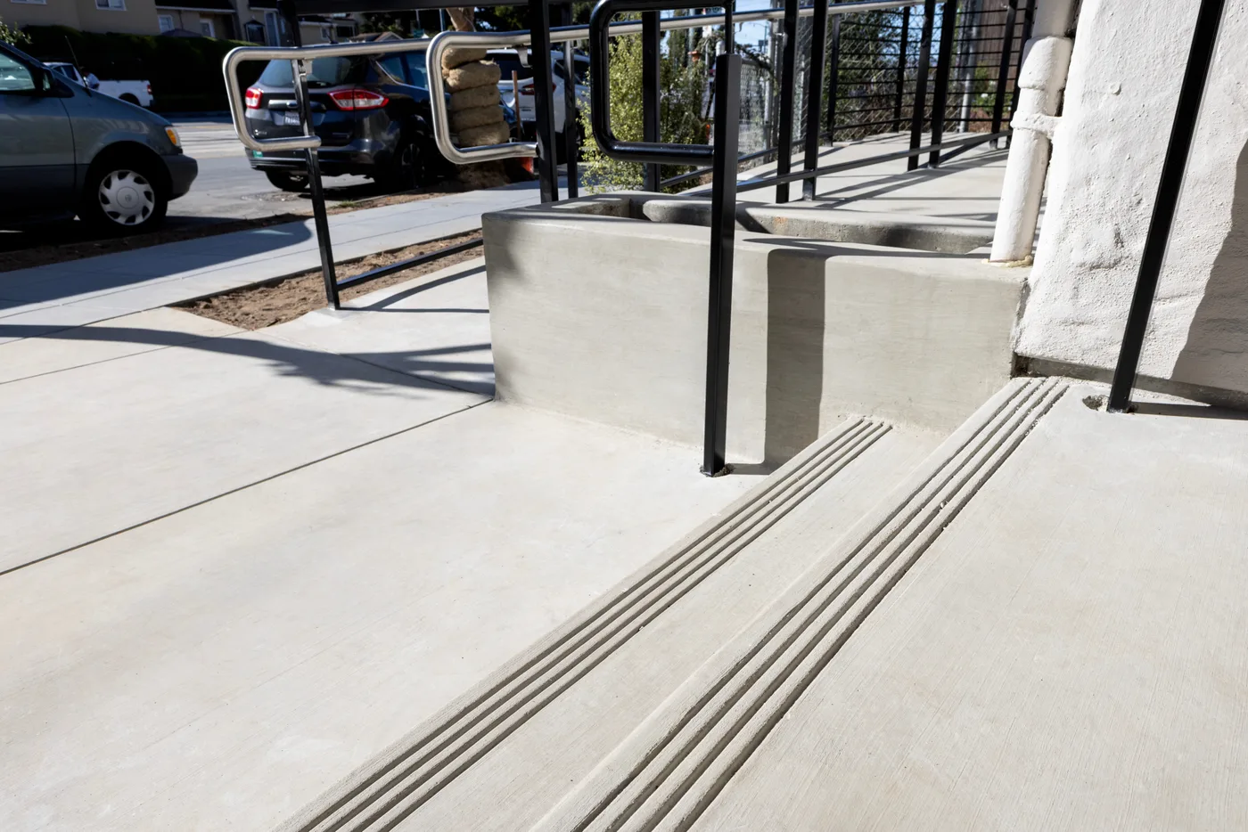 Detail where the ramp meets the walkway — tooled grooves, planter curbs, black handrail post — ADA Ramp & Sidewalk — West Portal, West Portal, San Francisco
