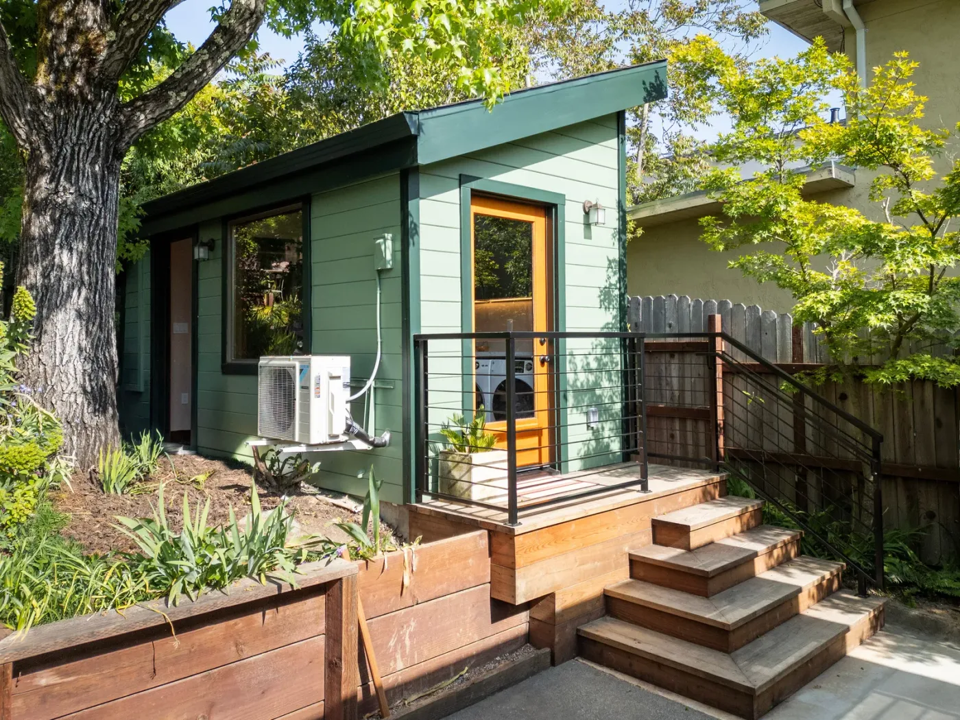 The finished 299 sq ft studio ADU — green siding, wood entry steps, mature tree — Backyard ADU Foundation, San Rafael, CA