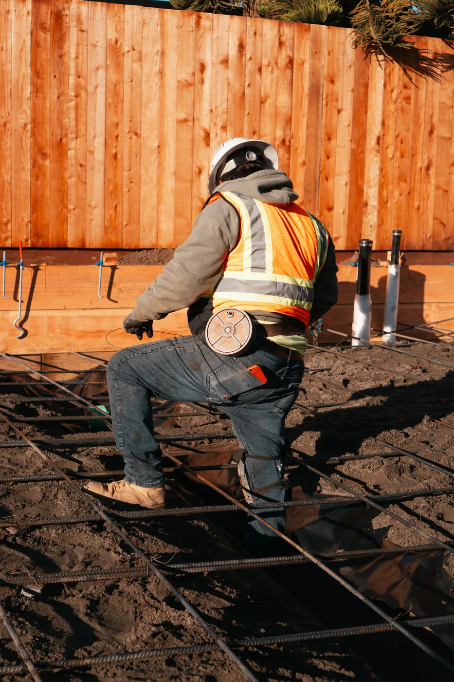 Ironworker tying the rebar mat over the vapor barrier along the new fence line — Berkeley Backyard Detached ADU, Berkeley, CA
