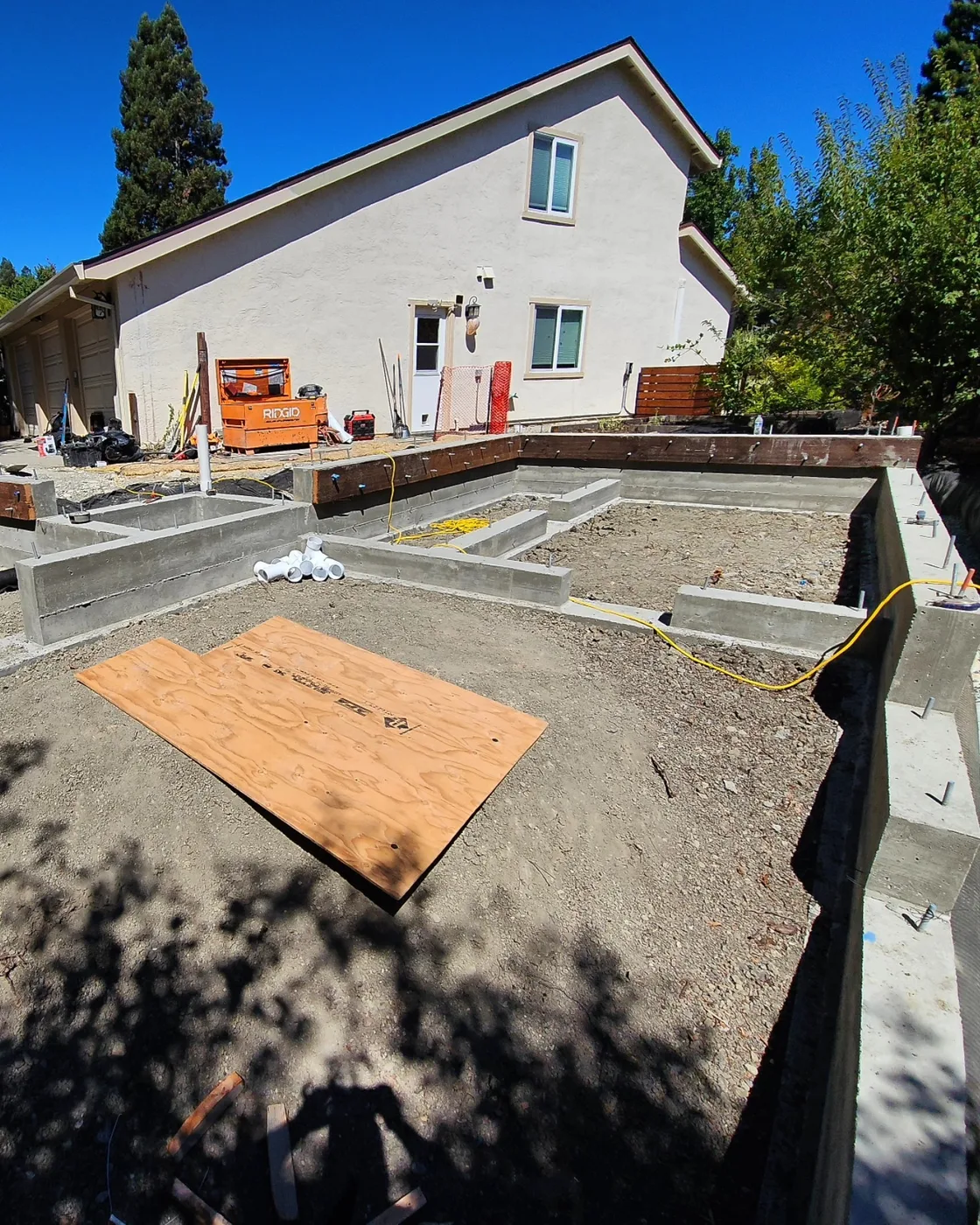 Stripped stem walls curing beside the main house, plumbing stubbed up — Danville ADU Foundation, Danville, CA
