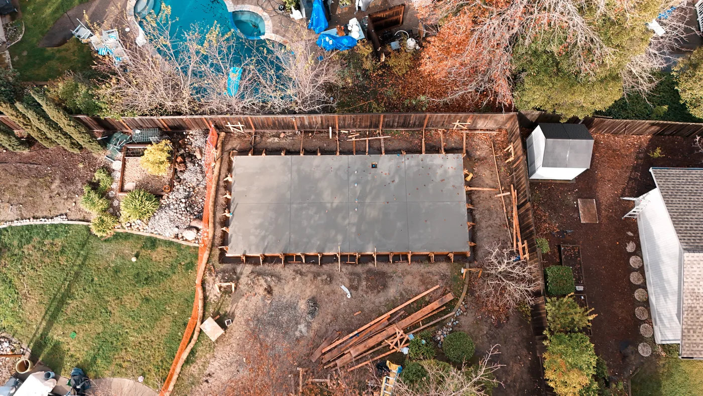 Top-down aerial of the cured slab in its forms, garden shed and pool alongside — Moraga Backyard ADU, Moraga, CA