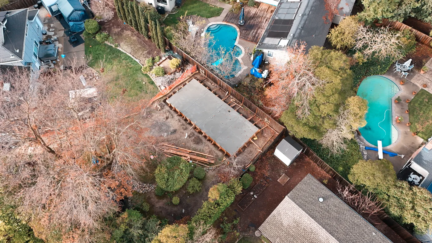 Wide aerial of the backyard slab set among the neighboring Moraga homes and pools — Moraga Backyard ADU, Moraga, CA