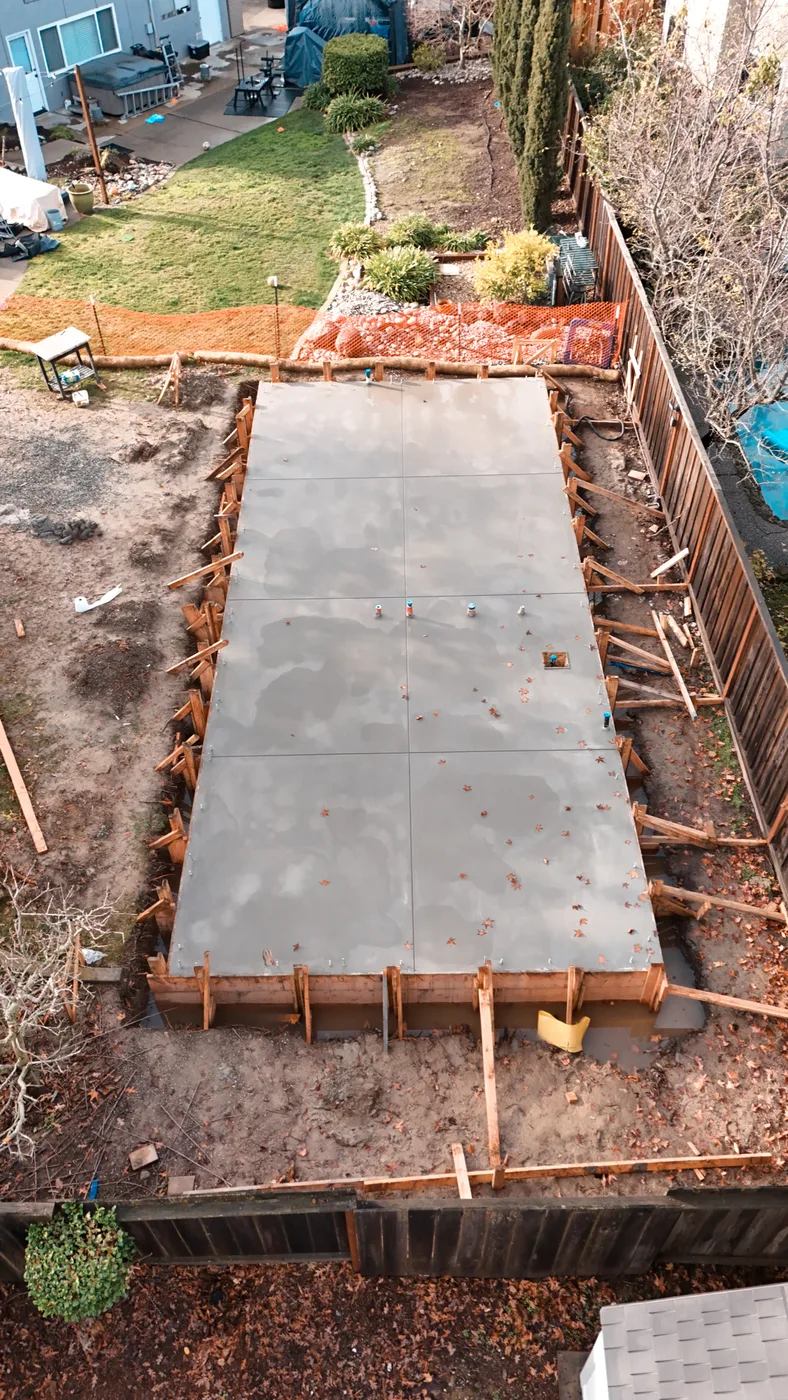 Aerial down the length of the cured slab toward the main house and lawn — Moraga Backyard ADU, Moraga, CA