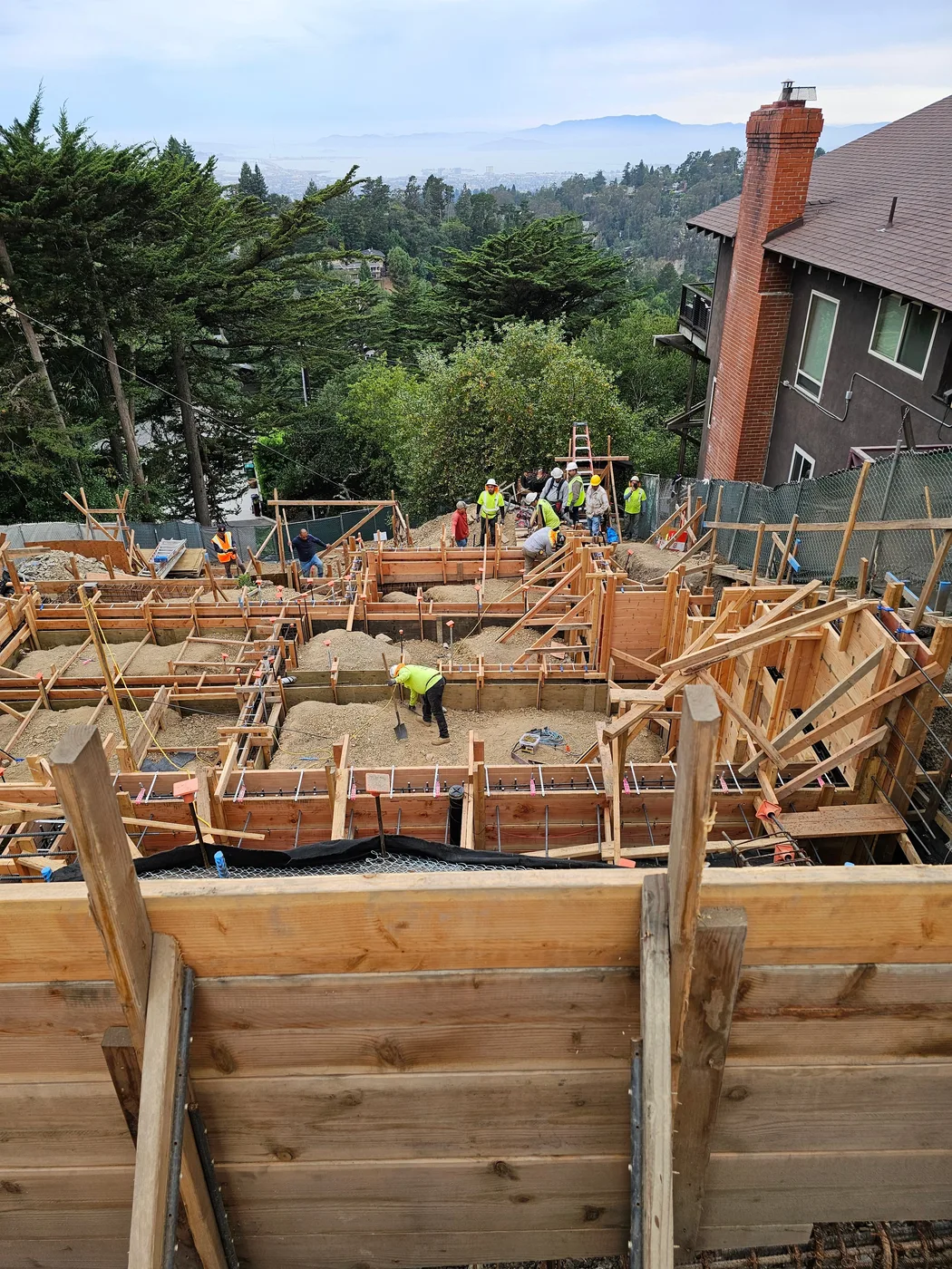 Formed foundation walls and rebar with the crew, house behind — Oakland Hills Custom Home, Oakland, CA