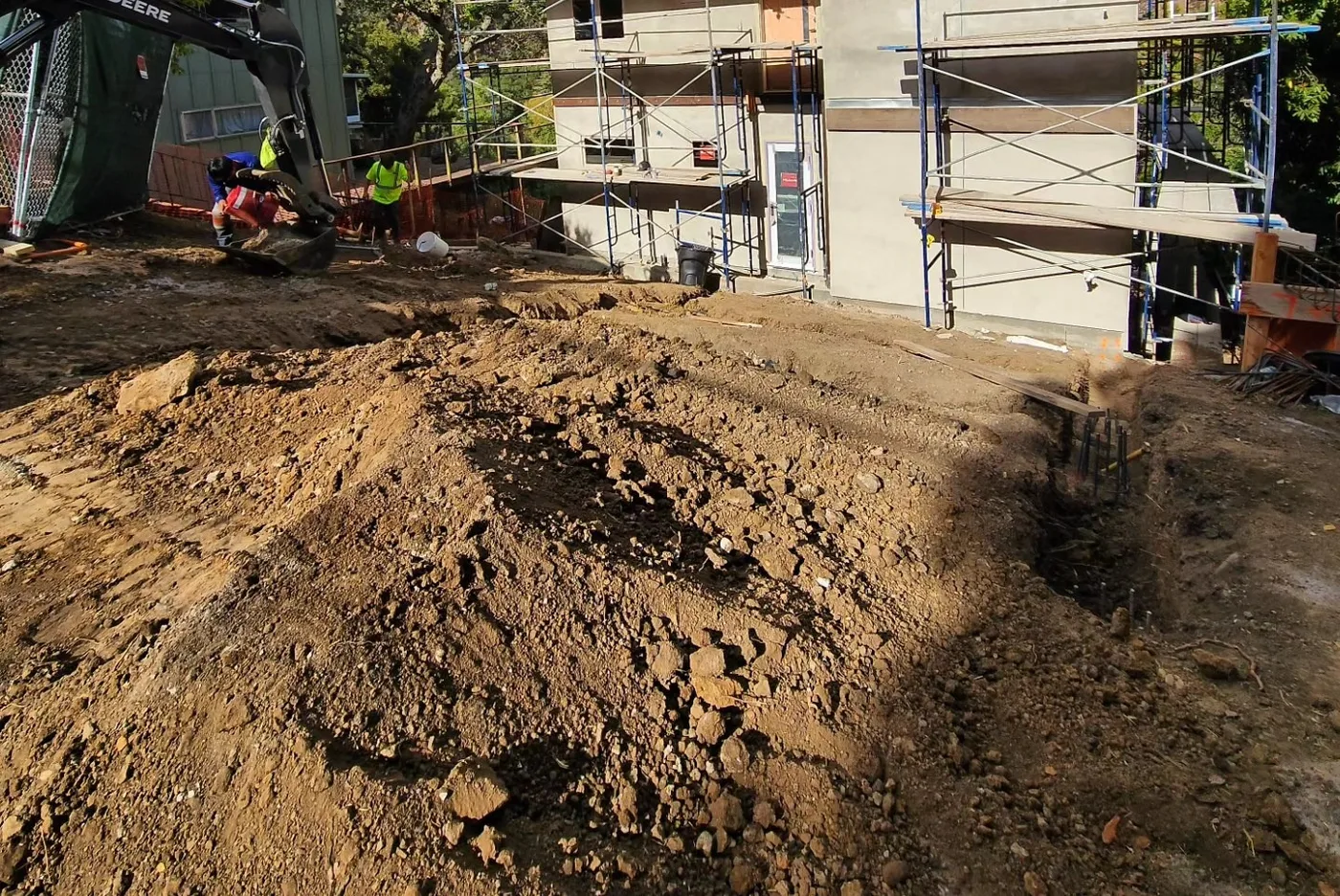 Excavator digging the foundation footings beside the home, scaffolding up — Richmond Bridge Driveway, Richmond, CA